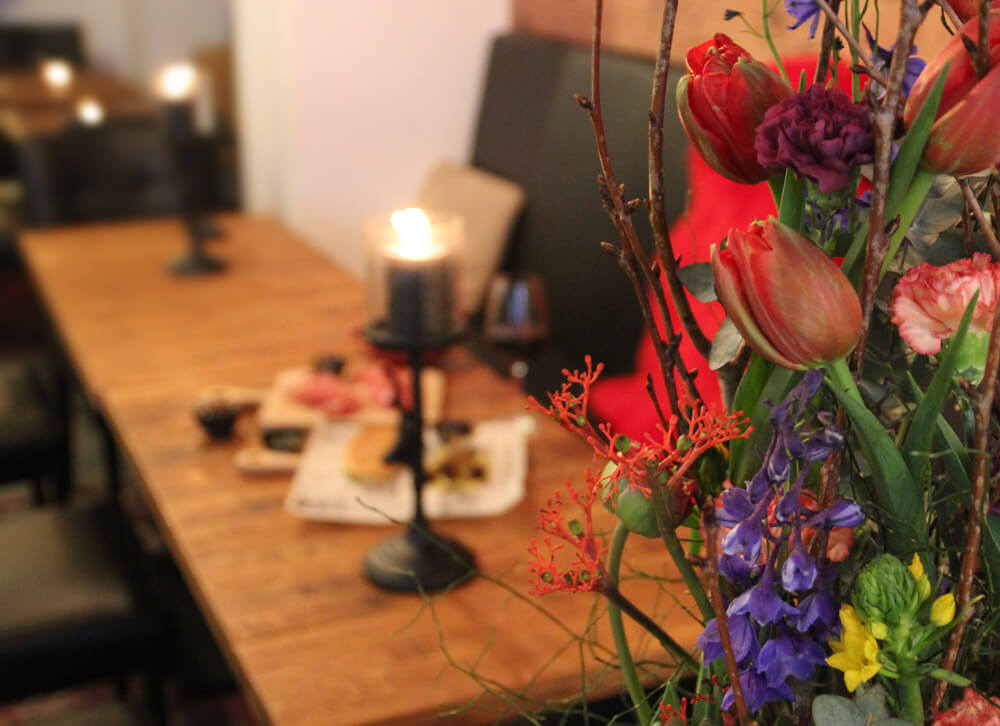 Kommunionsfeier / Konfirmationsfeier in der Byliny Mietbar in Düsseldorf planen, auf dem Bild feierliche Stimmung mit Holztisch, Blumen und Kerzen